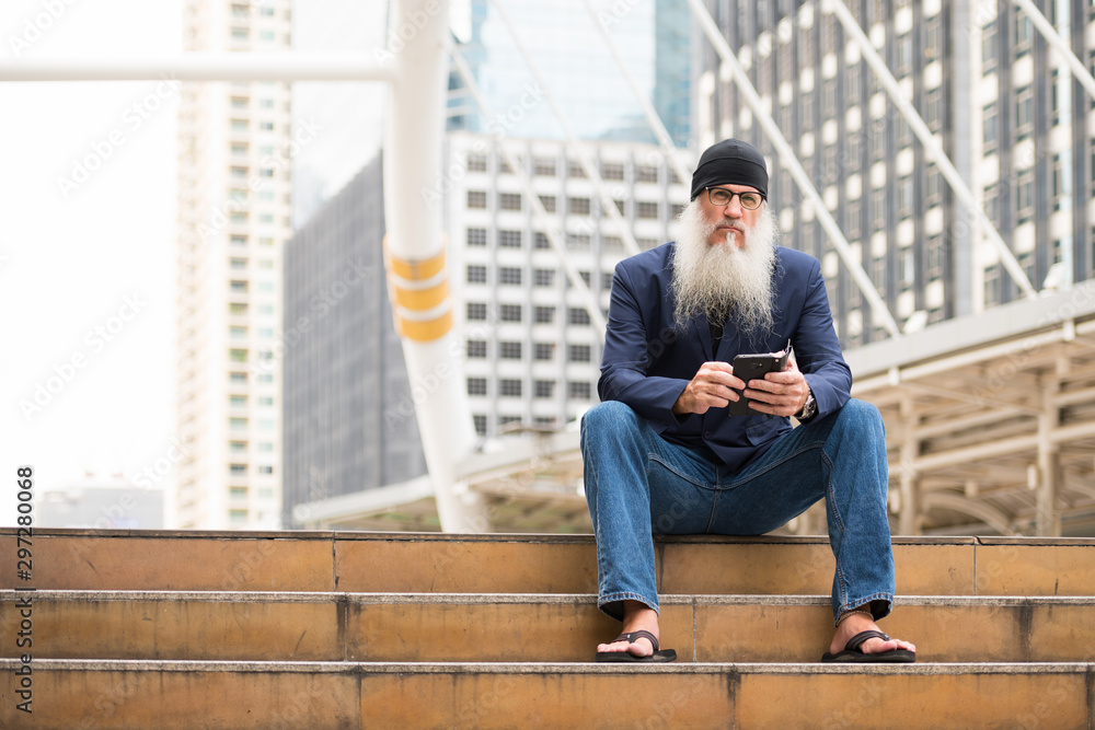 Mature bearded businessman sitting while using phone in the city outdoors Mature bearded businessman sitting while using phone in the city outdoors