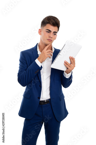 young thoughtful businessman looking at a white tablet mobile. He is wearing a blue jacket suit and a white shirt. He is in a photo studio.