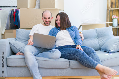 Young couple sitting on the sofa at new home using computer laptop, smiling happy for moving to a new apartment
