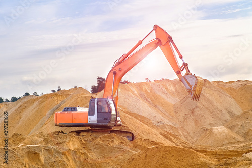 Crawler excavator works at a construction site on sunset background. Heavy construction equipment on a background of mountains of sand. A machine drips sand with a bucket.