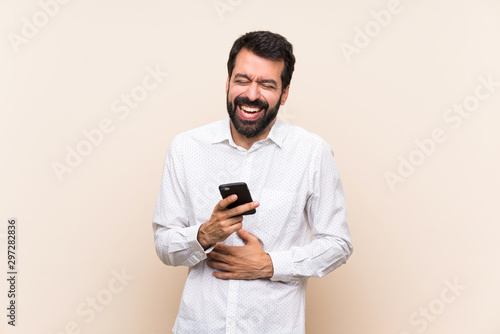 Young man with beard holding a mobile smiling a lot