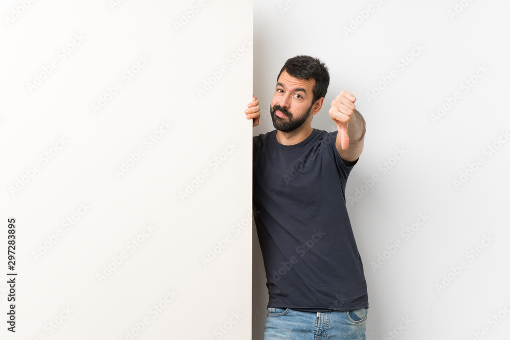 Young handsome man with beard holding a big empty placard showing thumb down with negative expression Young handsome man with beard holding a big empty placard showing thumb down with negative expression