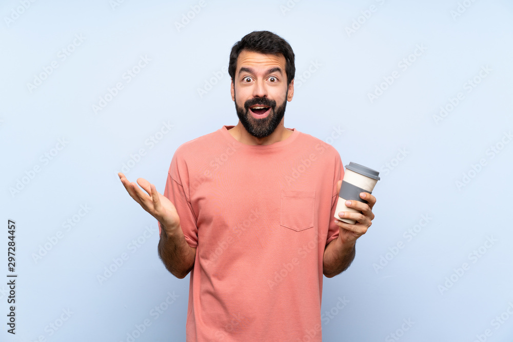 Young man with beard holding a take away coffee over isolated blue background with shocked facial expression Young man with beard holding a take away coffee over isolated blue background with shocked facial expression