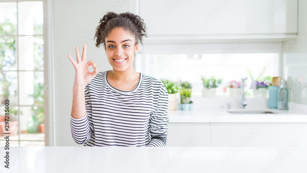 Beautiful african american woman with afro hair wearing casual striped sweater smiling positive doing ok sign with hand and fingers. Successful expression. Beautiful african american woman with afro hair wearing casual striped sweater smiling positive doing ok sign with hand and fingers. Successful expression.