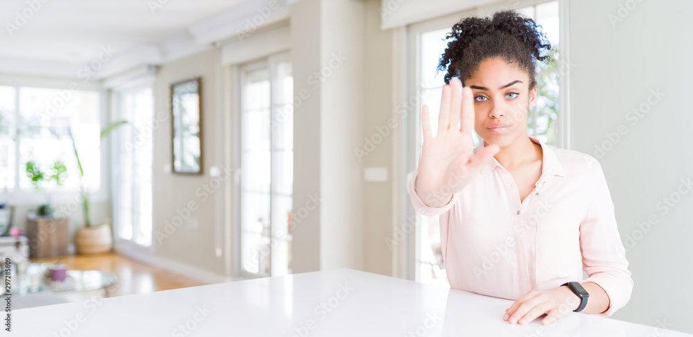 Wide angle of beautiful african american woman with afro hair doing stop sing with palm of the hand. Warning expression with negative and serious gesture on the face.