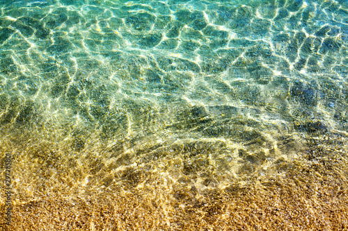 Golden sand under clear blue sea water and sunlight glow reflection close up top view, yellow sandy beach texture below transparent ocean surface background, abstract natural seaside pattern backdrop