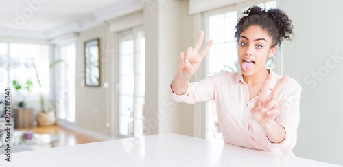 Wide angle of beautiful african american woman with afro hair smiling with tongue out showing fingers of both hands doing victory sign. Number two.