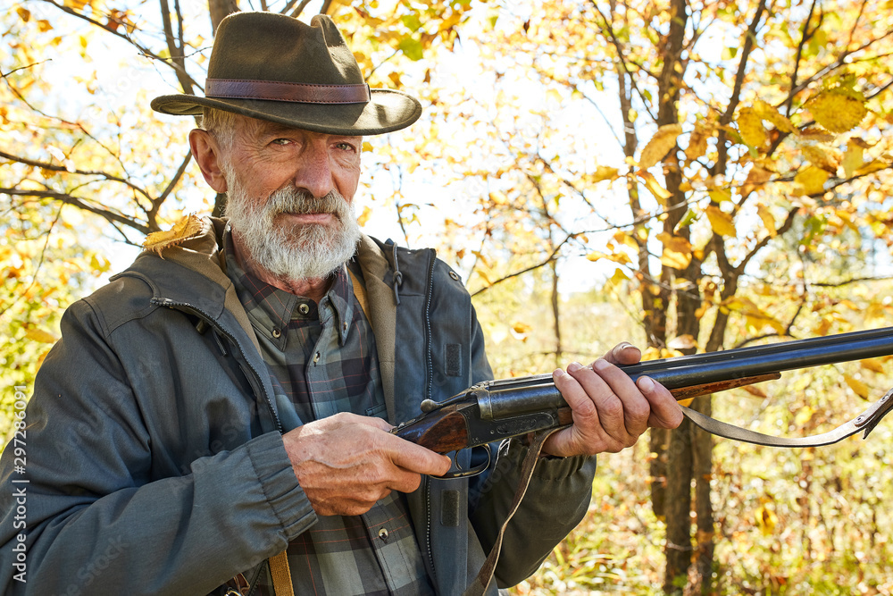 Fototapeta premium Senior caucasian hunter jolding shotgun ready to shoot on wild animals, shoot on bird in forest.