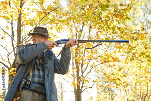 Concentrated hunter holding rifle and waiting for prey, hunter shooting in autumn forest. Hunting season