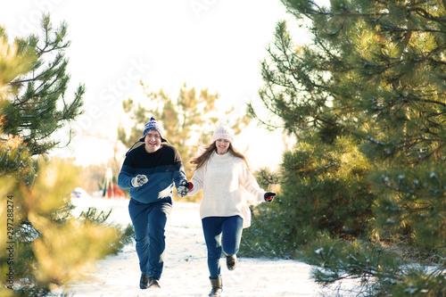 A loving couple holding hands runs through the winter forest. Laugh and have a good time