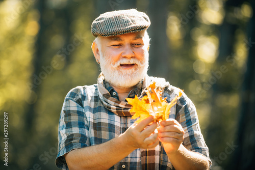 Portrait of a senior autumn man outdoors. Happy senior man hiking in autumn in nature. Golden age grandfather. Grandfather relaxing in autumn park. © Volodymyr