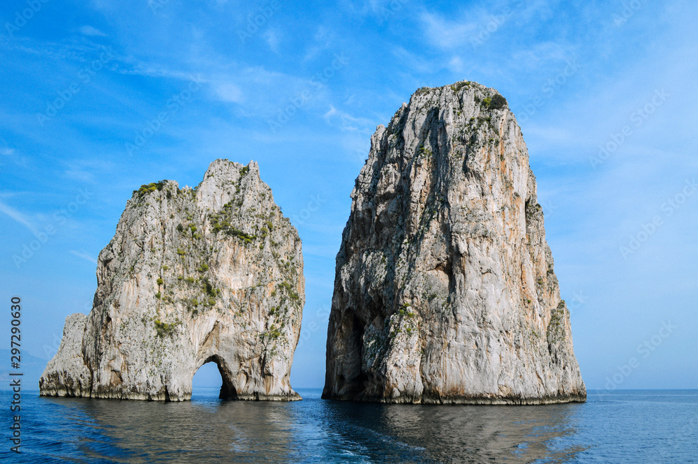 The picturesque cliffs of Faraglioni near the island of Capri on a background of blue sea and sky.