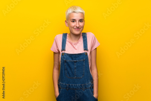 Teenager girl with overalls on yellow background laughing
