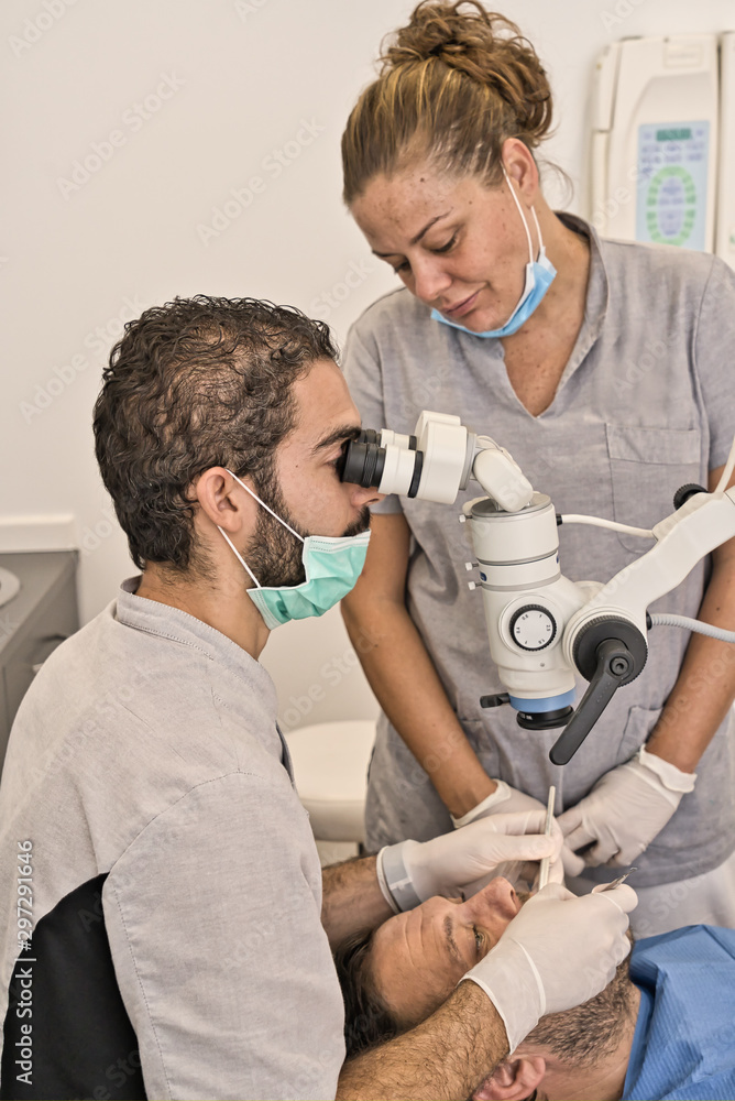 Fototapeta premium Dental doctor with microscope and blue mask next to his assistant checking his patient's dental health in a modern clinic