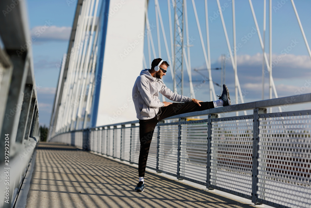 Young athlete man stretching his muscles before running on bridge on sunny day Young athlete man stretching his muscles before running on bridge on sunny day