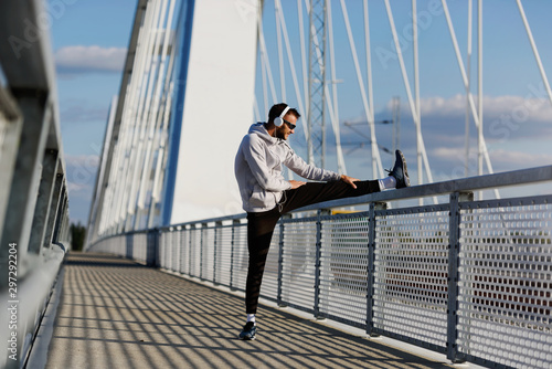 Young athlete man stretching his muscles before running on bridge on sunny day