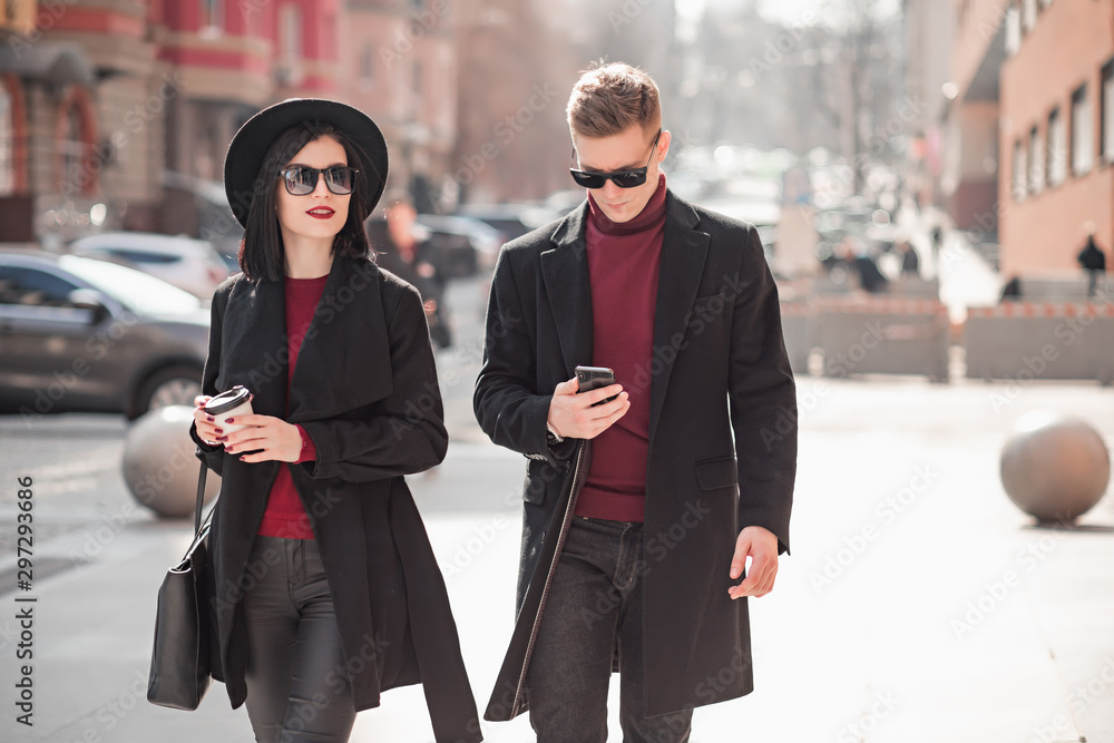 handsome young man and beautiful young woman in a black coat go and look at the phone on the street handsome young man and beautiful young woman in a black coat go and look at the phone on the street