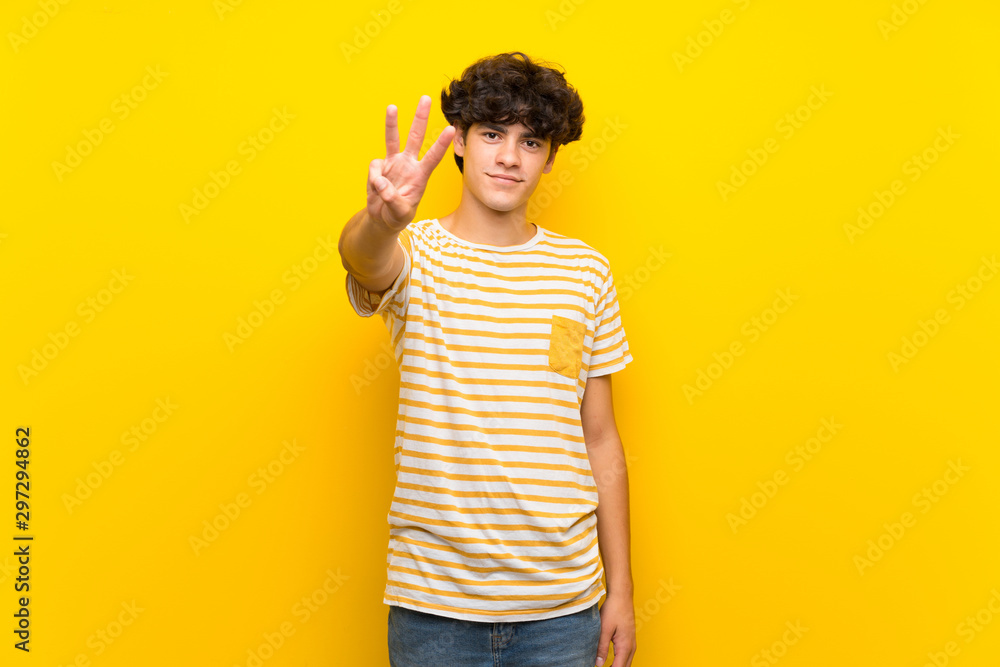 Young man over isolated yellow wall happy and counting three with fingers Young man over isolated yellow wall happy and counting three with fingers