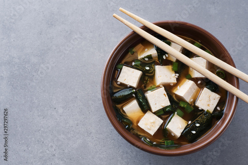 Bowl with miso soup and chopsticks on a gray background.