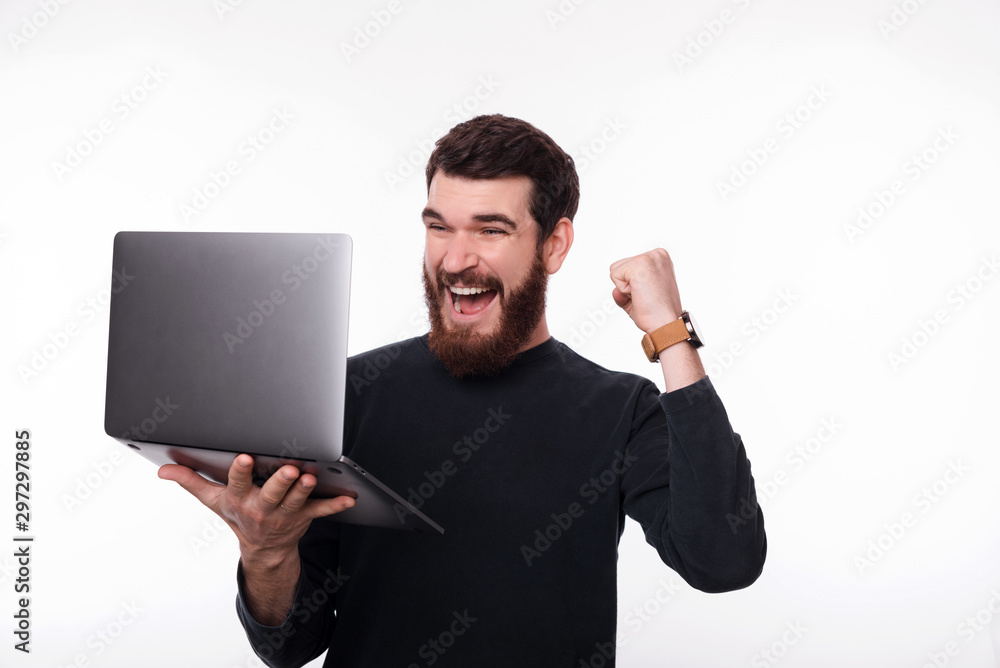 Photo of smiling man celebrate victory and holding laptop over white background Photo of smiling man celebrate victory and holding laptop over white background