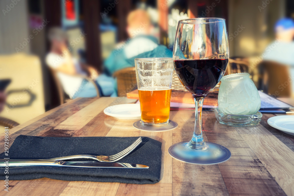 A glass of wine and beer on the table with blurry people sitting in the restaurant background.
