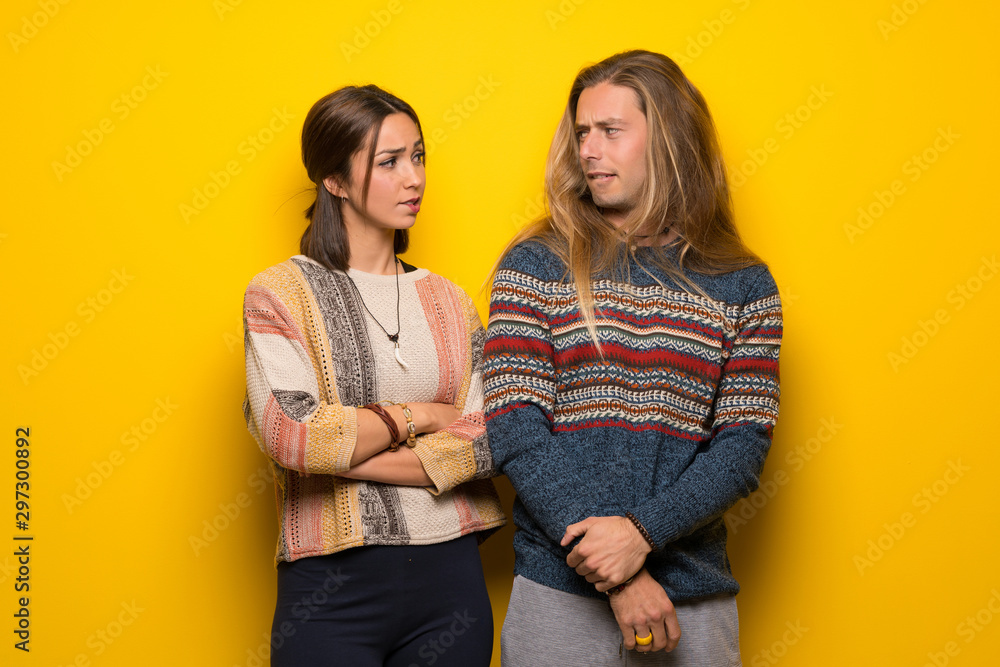 Hippie couple over yellow background with confuse face expression while bites lip Hippie couple over yellow background with confuse face expression while bites lip