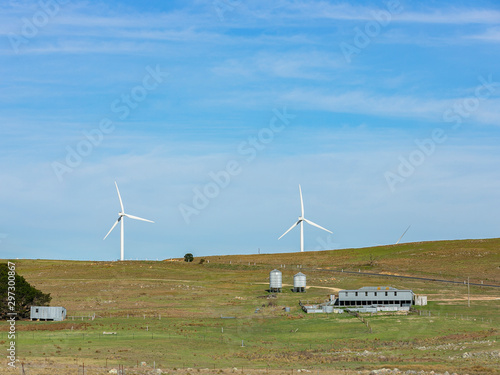 A pair of large wind turbines moving to create kinetic energy for renewable energy supply with a shack house in the foreground near Lake George and north of Bungendore in New South Wales, Australia 