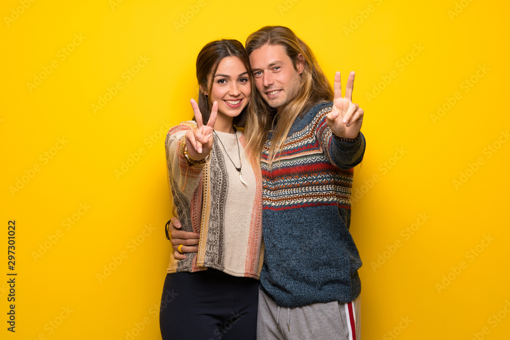Hippie couple over yellow background smiling and showing victory sign Hippie couple over yellow background smiling and showing victory sign