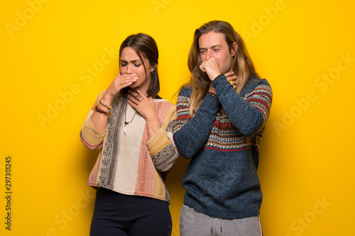 Hippie couple over yellow background is suffering with cough and feeling bad