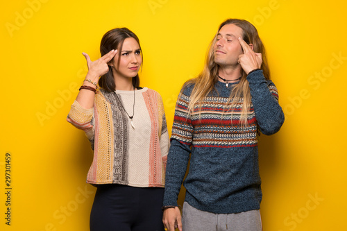 Hippie couple over yellow background with problems making suicide gesture