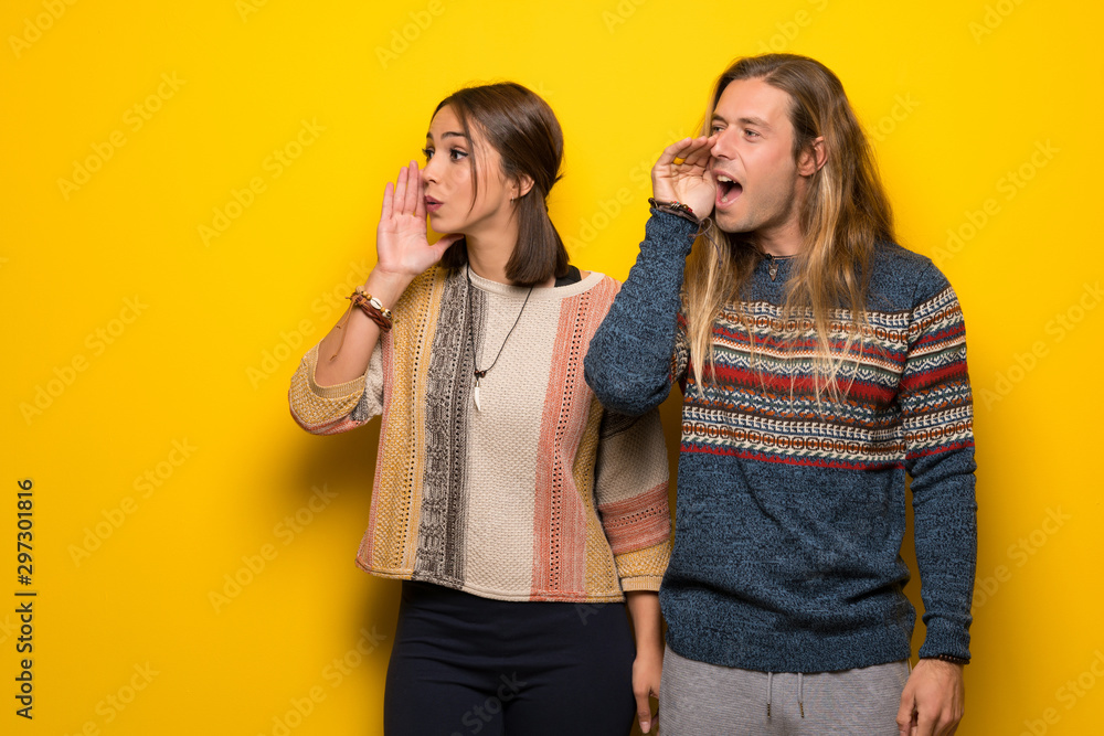 Hippie couple over yellow background shouting with mouth wide open to the lateral Hippie couple over yellow background shouting with mouth wide open to the lateral