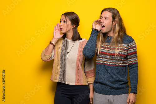 Hippie couple over yellow background shouting with mouth wide open to the lateral