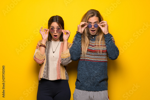 Hippie couple over yellow background with glasses and surprised © luismolinero