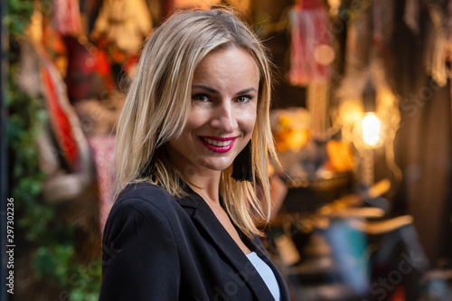 Blonde, beautiful woman at the shop window on the street in the evening light - image