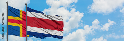 Aland Islands and Costa Rica flag waving in the wind against white cloudy blue sky together. Diplomacy concept, international relations.