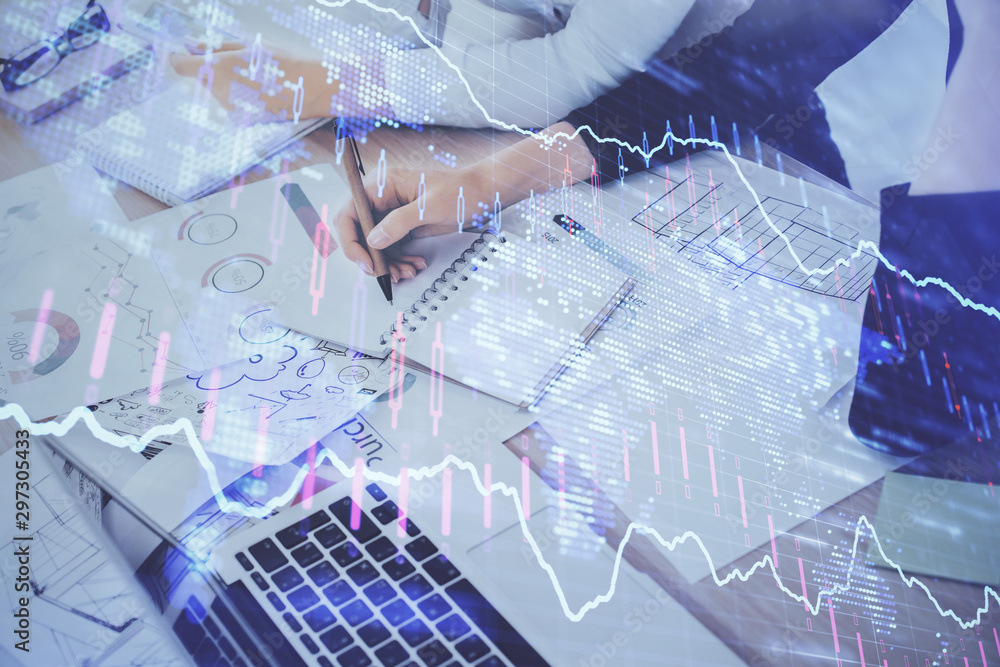 A woman hands writing information about stock market in notepad. Forex chart holograms in front. Concept of research. Double exposure A woman hands writing information about stock market in notepad. Forex chart holograms in front. Concept of research. Double exposure