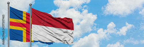 Aland Islands and Indonesia flag waving in the wind against white cloudy blue sky together. Diplomacy concept, international relations.