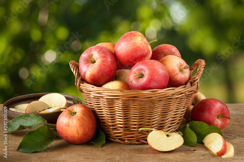Ripe red-yellow apples with leaves in a basket on a wooden table. Whole and sliced fruits. Harvest fruit trees.