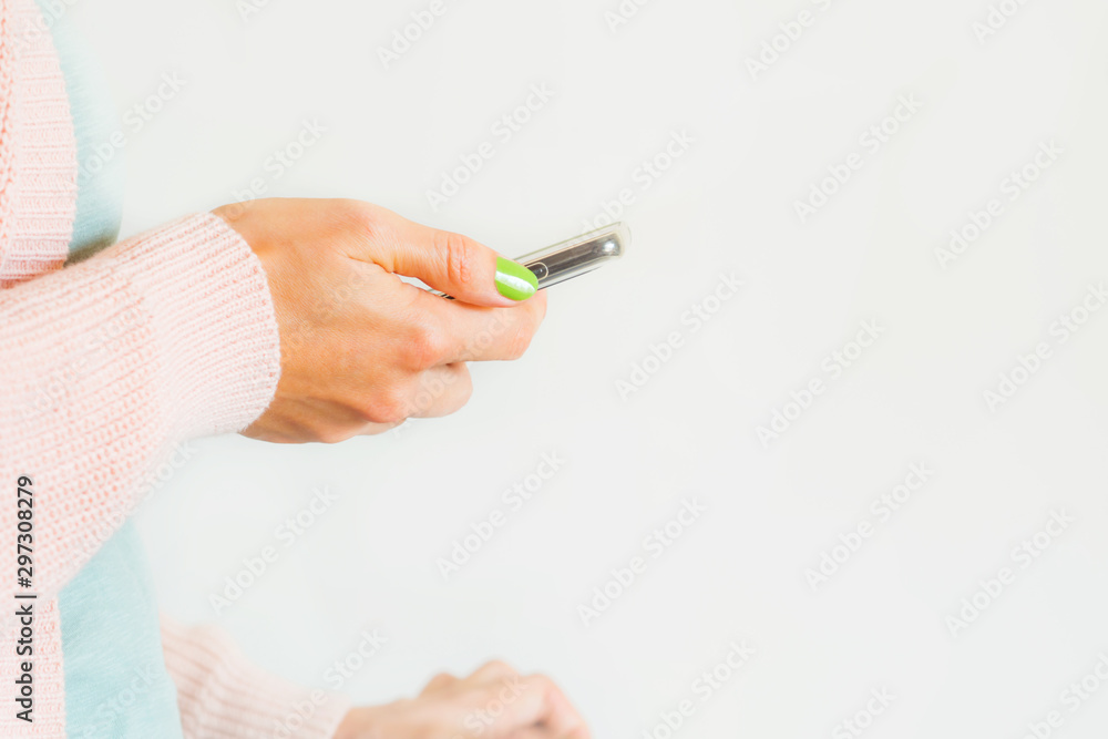 Young woman wearing pastel pink and green mint clothes using mobile phone. Closeup on hand. Copy space on white Young woman wearing pastel pink and green mint clothes using mobile phone. Closeup on hand. Copy space on white
