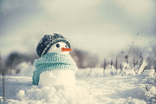 Little cute snowman in a knitted hat and scarf on snow on a sunny winter day, toned. Christmas card © isavira