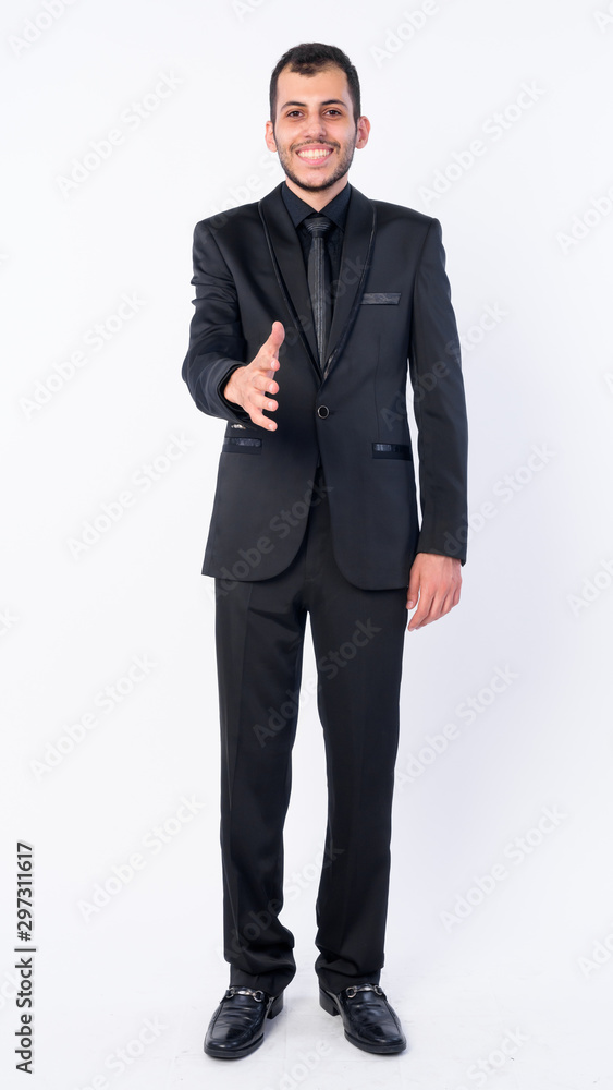 Full body shot of happy young bearded Persian businessman in suit giving handshake Full body shot of happy young bearded Persian businessman in suit giving handshake