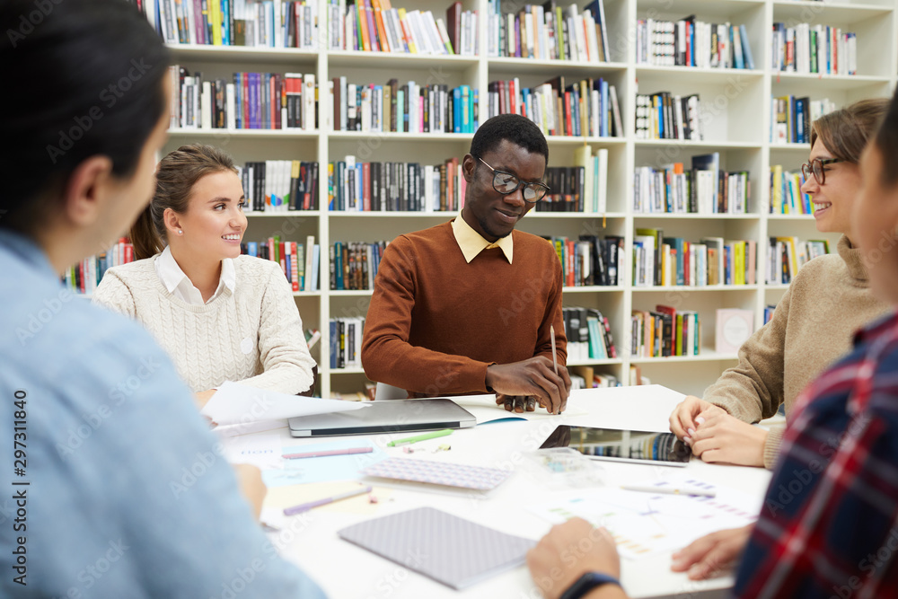 Multi-ethnic group of students sharing ideas while discussing team project during meeting in college library, copy space Multi-ethnic group of students sharing ideas while discussing team project during meeting in college library, copy space