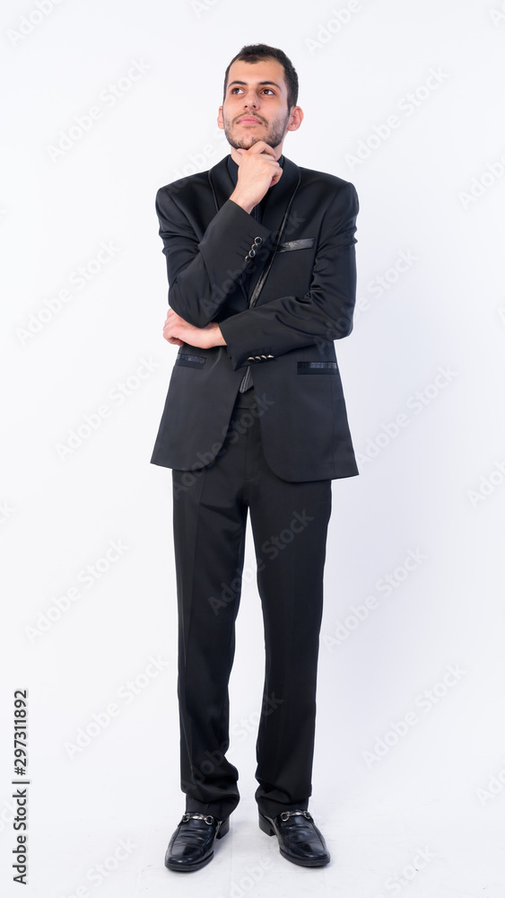 Full body shot of young bearded Persian businessman in suit thinking Full body shot of young bearded Persian businessman in suit thinking