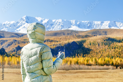  Woman drink tea on nature in autumn.  A young tourist woman drinks a hot drink from a cup and enjoys the scenery in the mountains. Trekking travel concept. © Sergey
