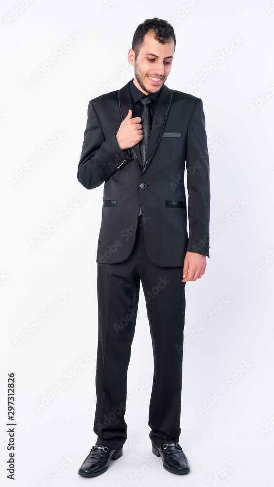 Full body shot of happy young bearded Persian businessman in suit looking down Full body shot of happy young bearded Persian businessman in suit looking down