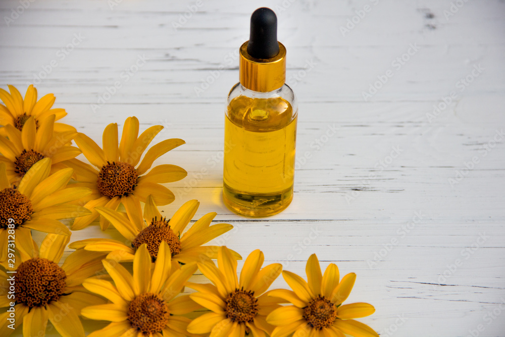 yellow flowers and cosmetic oil in a bottle on a wooden light background yellow flowers and cosmetic oil in a bottle on a wooden light background