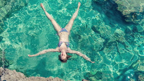 Young slender European girl in swimsuit swimming in clear blue transparent sea water. She enjoying her summer holidays.