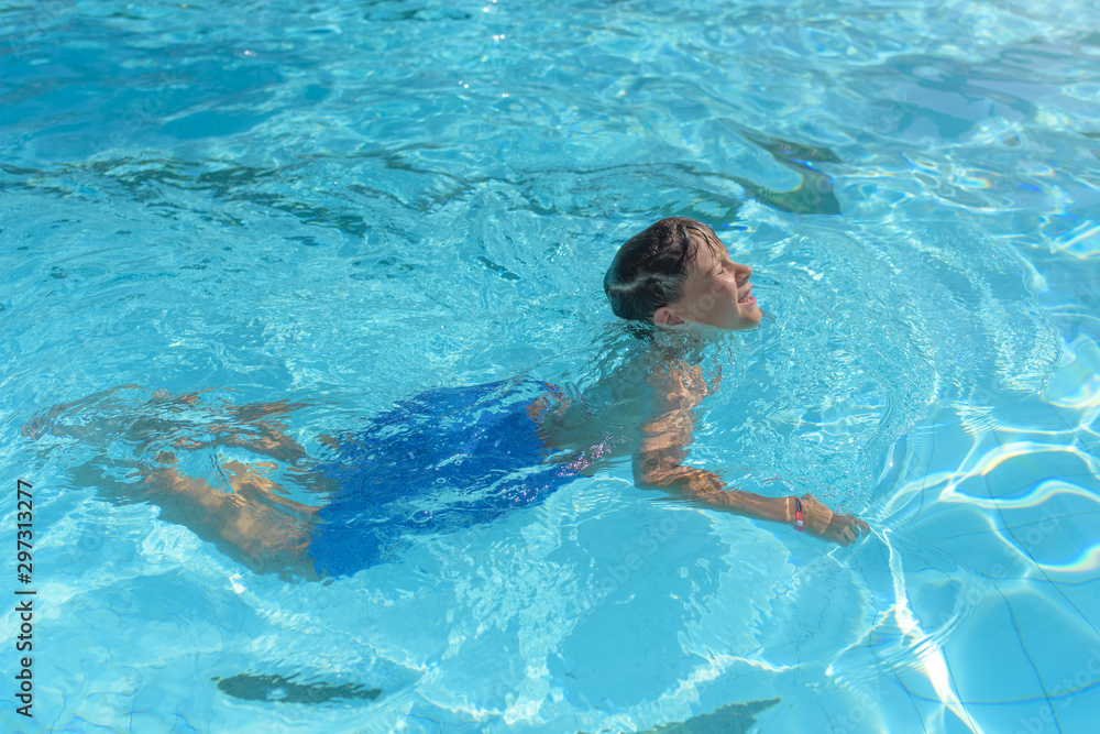 Portrait of cheerful European boy swimming in pool. He is enjoying his summer vacations.