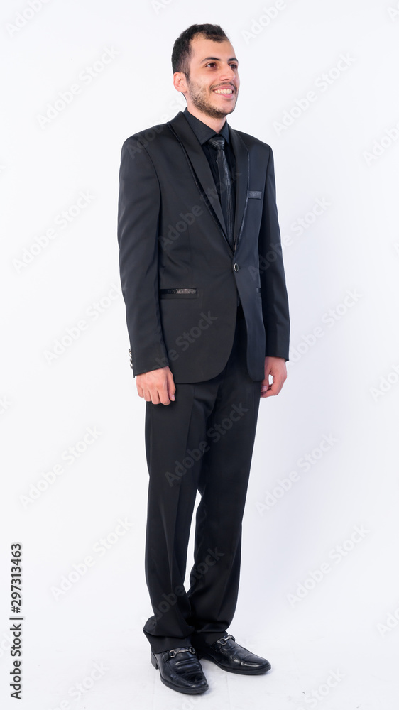 Full body shot of happy young bearded Persian businessman in suit thinking Full body shot of happy young bearded Persian businessman in suit thinking