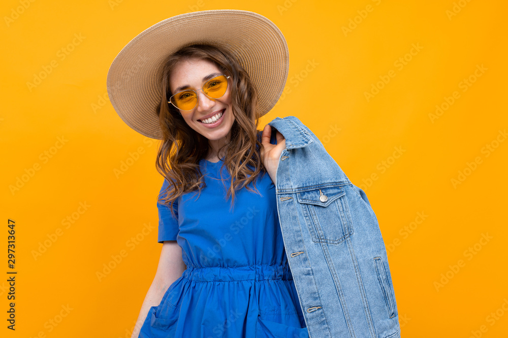 stylish brown-haired woman in yellow glasses and a blue dress on a background of a yellow wall stylish brown-haired woman in yellow glasses and a blue dress on a background of a yellow wall